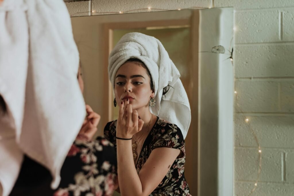 Woman with a towel wrap applying skincare in front of a mirror